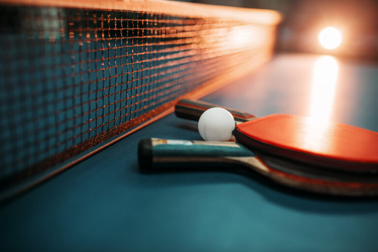 Two tennis rackets and ball against net on table